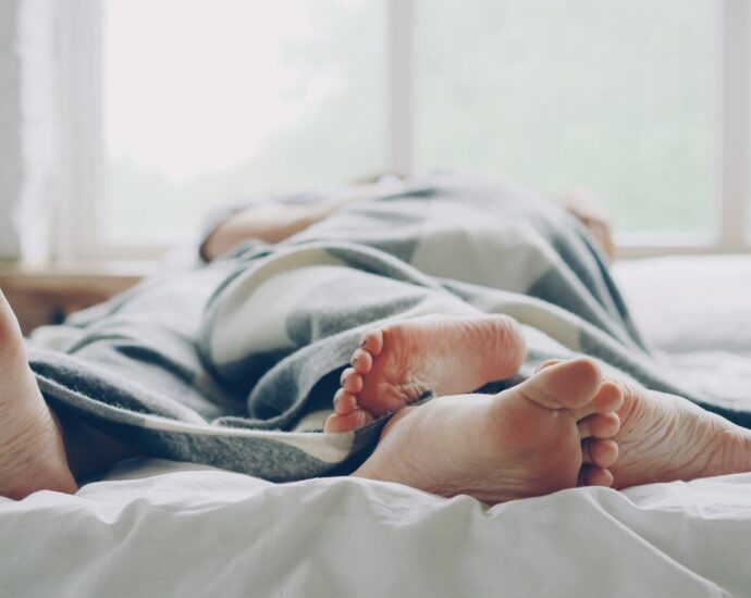 Two people lying in bed under a blanket, relaxing morning scene.