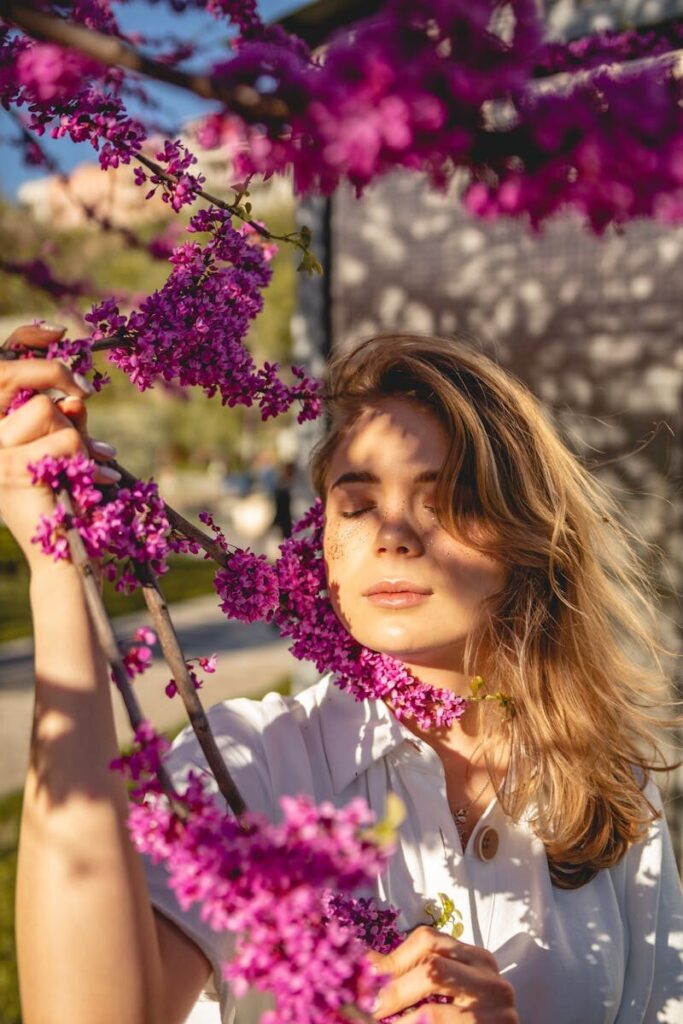 A woman with closed eyes embraces vibrant pink blossoms on a sunny spring day.