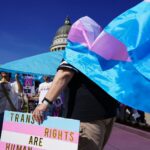 People holding transgender flag and sign at rally.