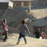 a couple of kids flying a kite on top of a hill