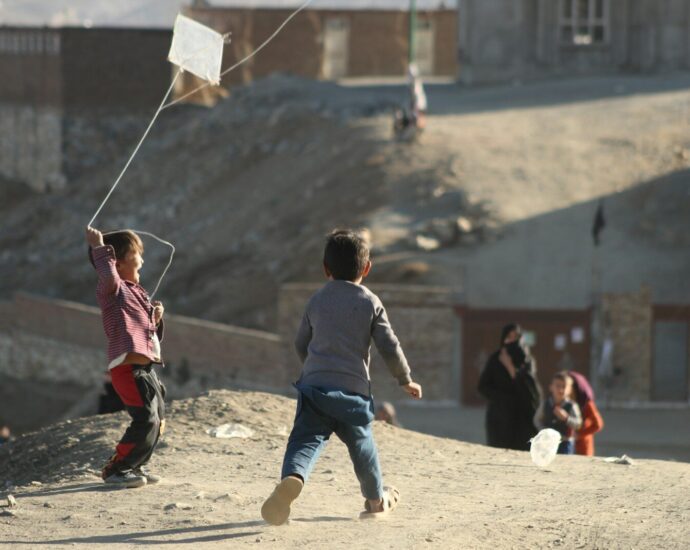 a couple of kids flying a kite on top of a hill