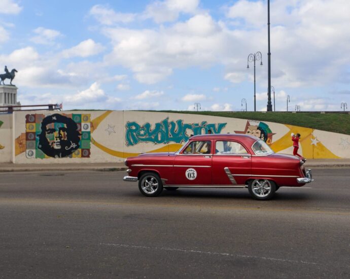 Vintage red car cruising by Cuban street art in Havana, featuring Che Guevara mural.