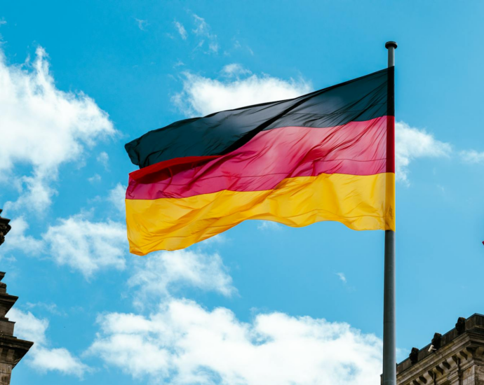 Vibrant German flag waving on a flagpole against a bright blue sky with clouds.