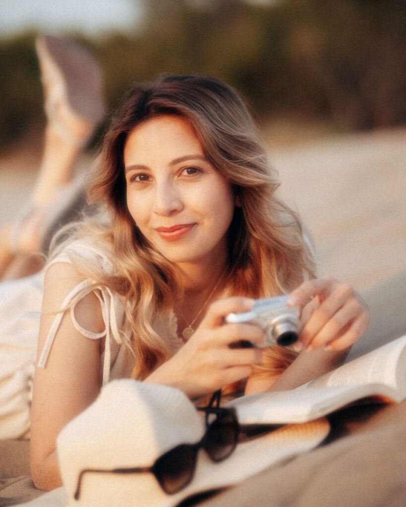 Young woman lying on beach sand holding a camera, enjoying the sunny day.