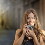 A cheerful woman with a vintage camera captures the moment on a sunlit urban street.