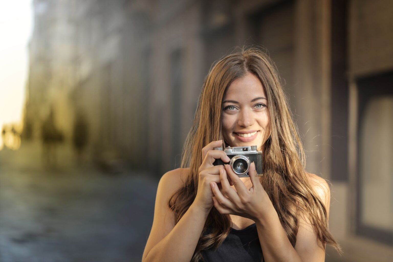 A cheerful woman with a vintage camera captures the moment on a sunlit urban street.