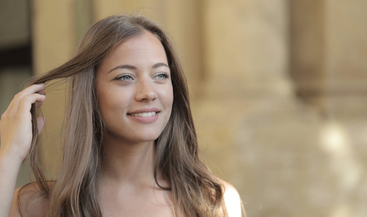 A young woman with long hair smiling while enjoying a sunny day outdoors.