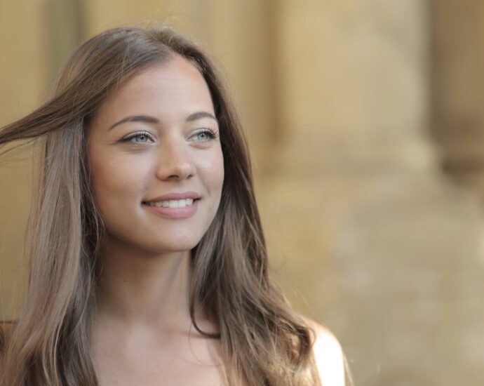 A young woman with long hair smiling while enjoying a sunny day outdoors.