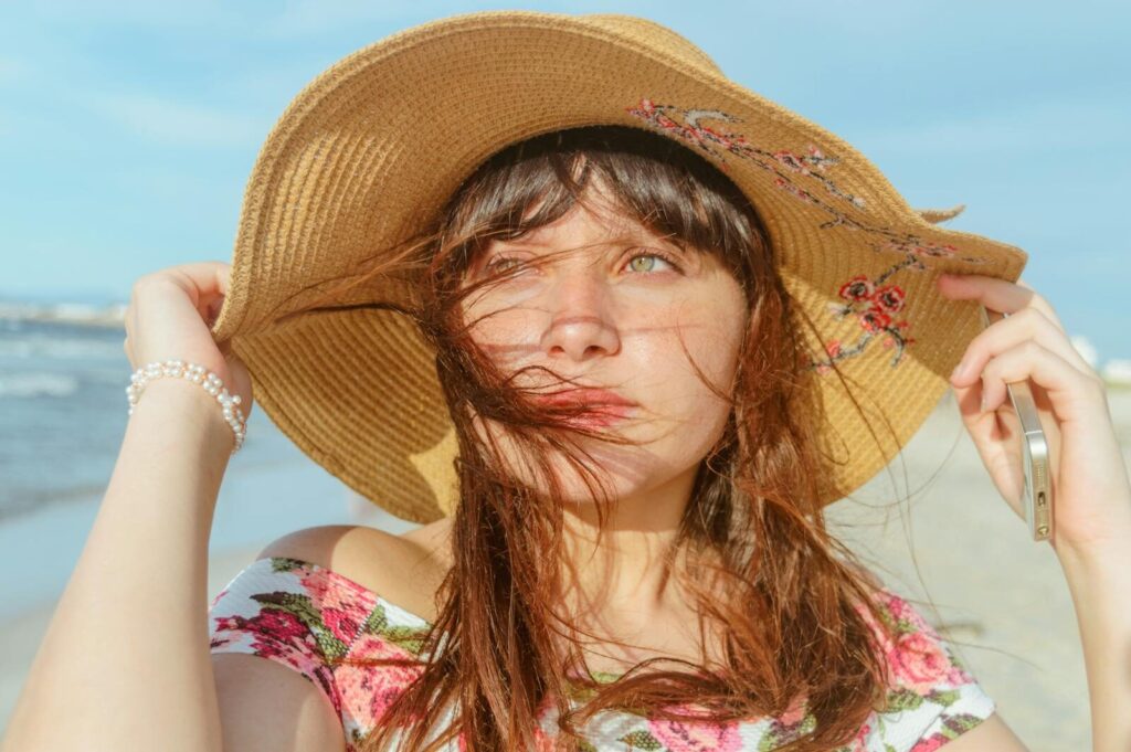 Young woman on the beach in a straw hat and floral top enjoying a sunny day.
