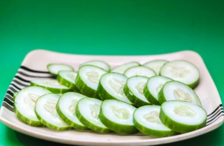 Close-up of sliced cucumbers arranged on a striped plate with a green background.