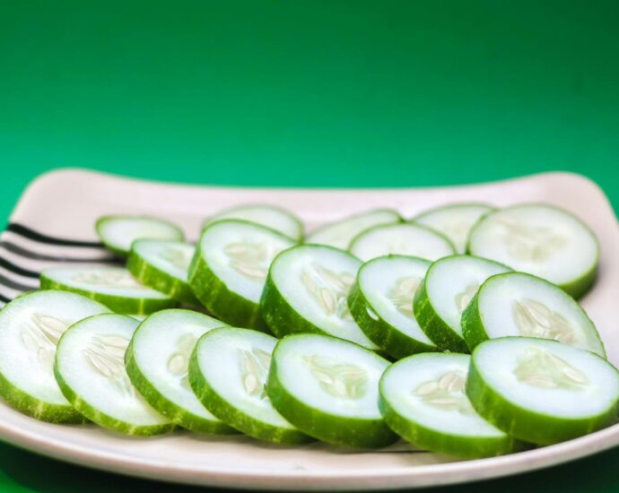 Close-up of sliced cucumbers arranged on a striped plate with a green background.