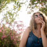 A woman in sunglasses enjoys a sunny day in a blooming garden, capturing tranquility.