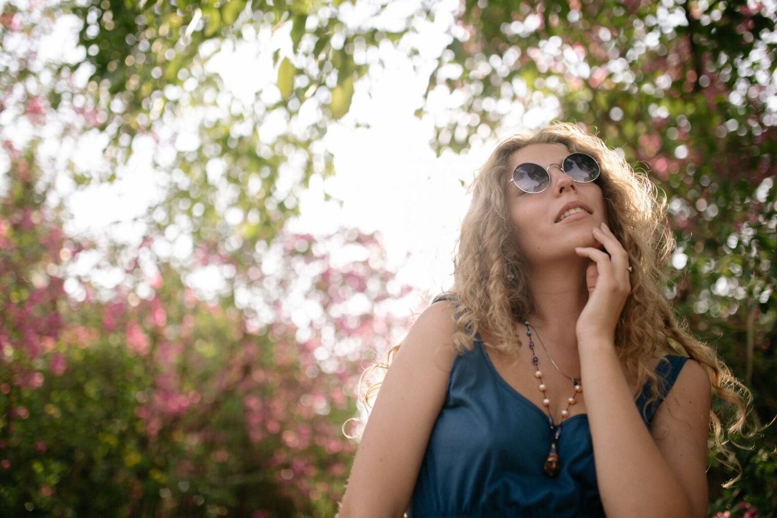 A woman in sunglasses enjoys a sunny day in a blooming garden, capturing tranquility.