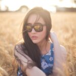 A serene portrait of a woman wearing sunglasses in a sunlit wheat field.