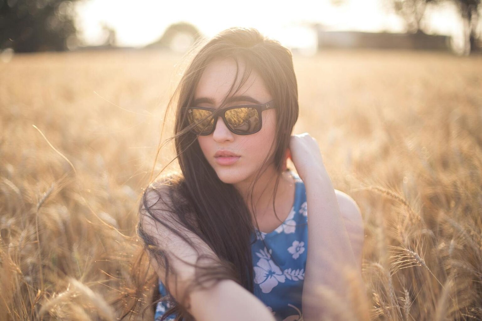 A serene portrait of a woman wearing sunglasses in a sunlit wheat field.