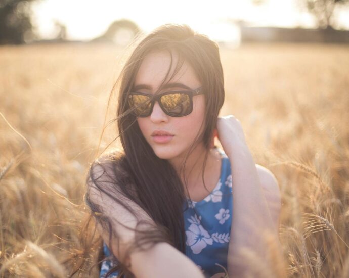 A serene portrait of a woman wearing sunglasses in a sunlit wheat field.