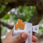 Close-up of a hand holding an open pack of cigarettes in a natural outdoor setting.