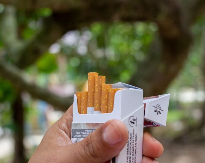 Close-up of a hand holding an open pack of cigarettes in a natural outdoor setting.