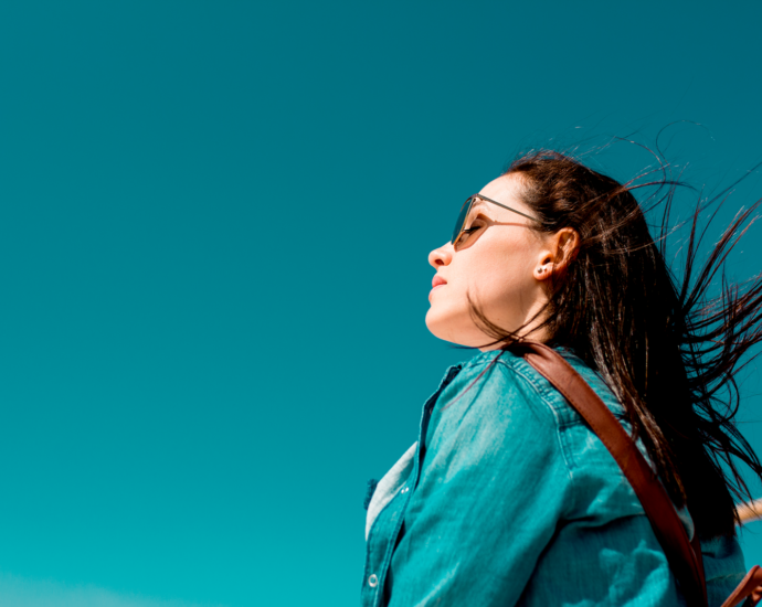 Fashionable woman outdoors in denim shirt with sunglasses under clear blue sky, enjoying sunny weather.
