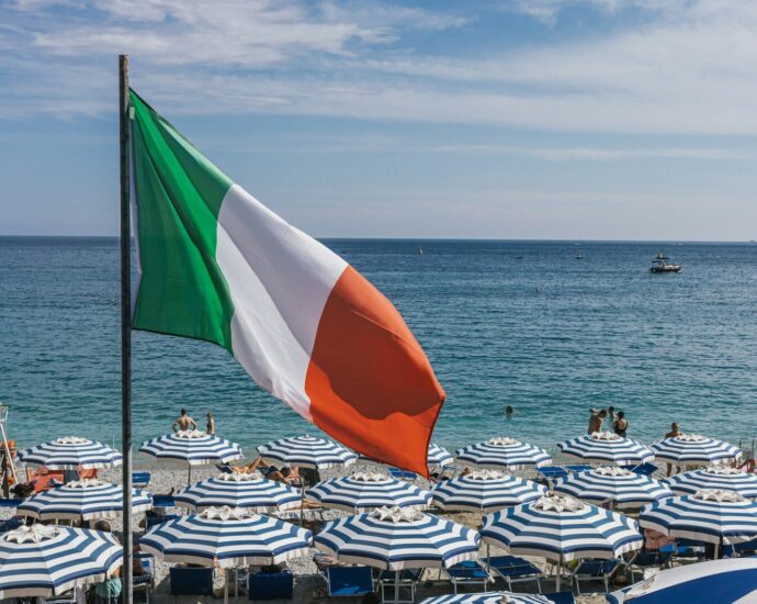 a large italian flag flying over a beach filled with umbrellas