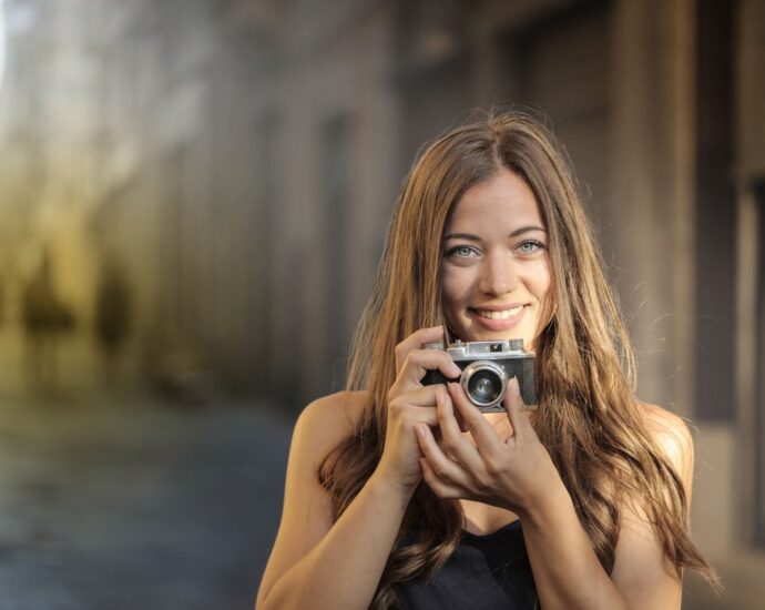 A cheerful woman with a vintage camera captures the moment on a sunlit urban street.