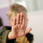 A child making a stop gesture with an open hand indoors.