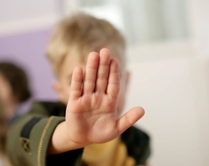 A child making a stop gesture with an open hand indoors.