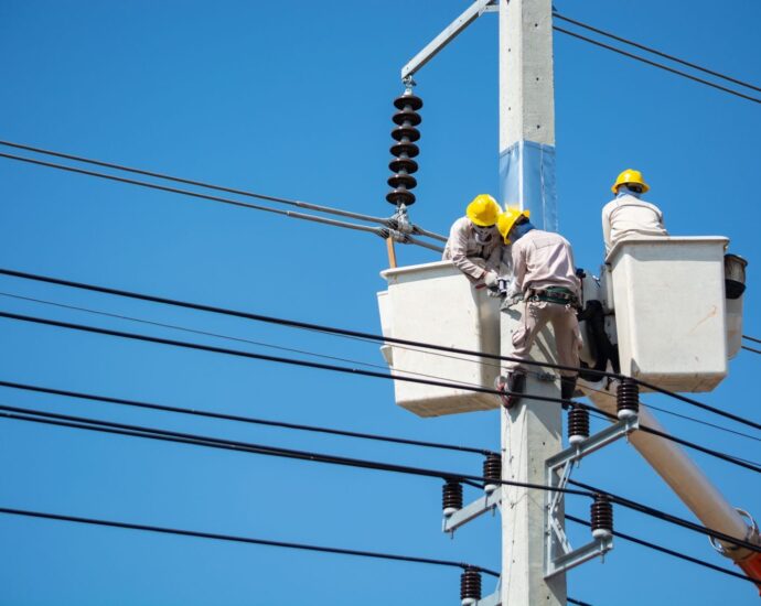 Electricians wearing safety gear work on power lines in Nakhon Ratchasima, Thailand.
