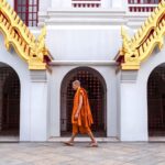 A Buddhist monk walks past the ornate architecture of Loha Prasat Temple in Bangkok, Thailand.