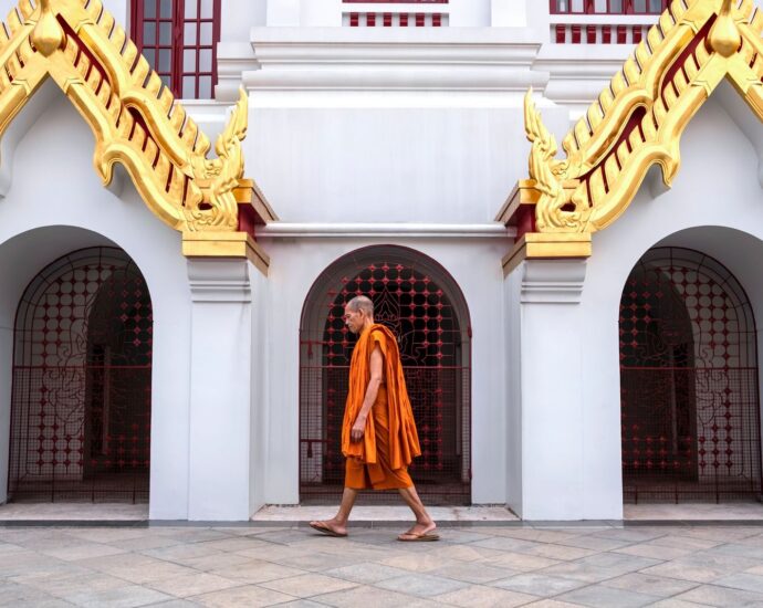 A Buddhist monk walks past the ornate architecture of Loha Prasat Temple in Bangkok, Thailand.