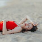 A woman in a red dress lying on a sandy beach, exuding relaxation and summer vibes.