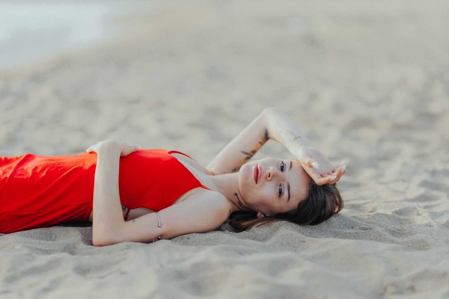 A woman in a red dress lying on a sandy beach, exuding relaxation and summer vibes.
