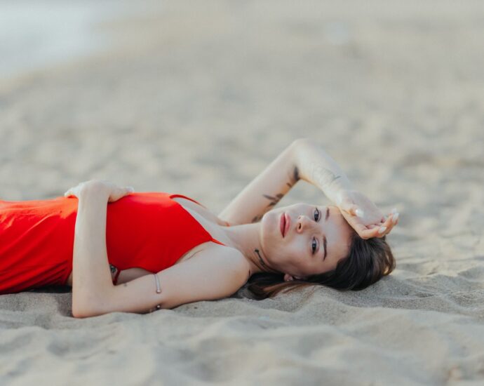 A woman in a red dress lying on a sandy beach, exuding relaxation and summer vibes.