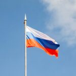 A russian flag waves against a blue sky.