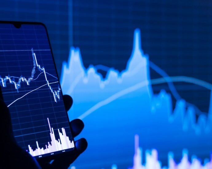 a person holding a cell phone in front of a stock chart