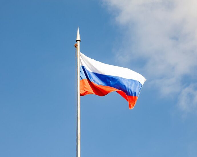 The russian flag waves against a clear, blue sky.
