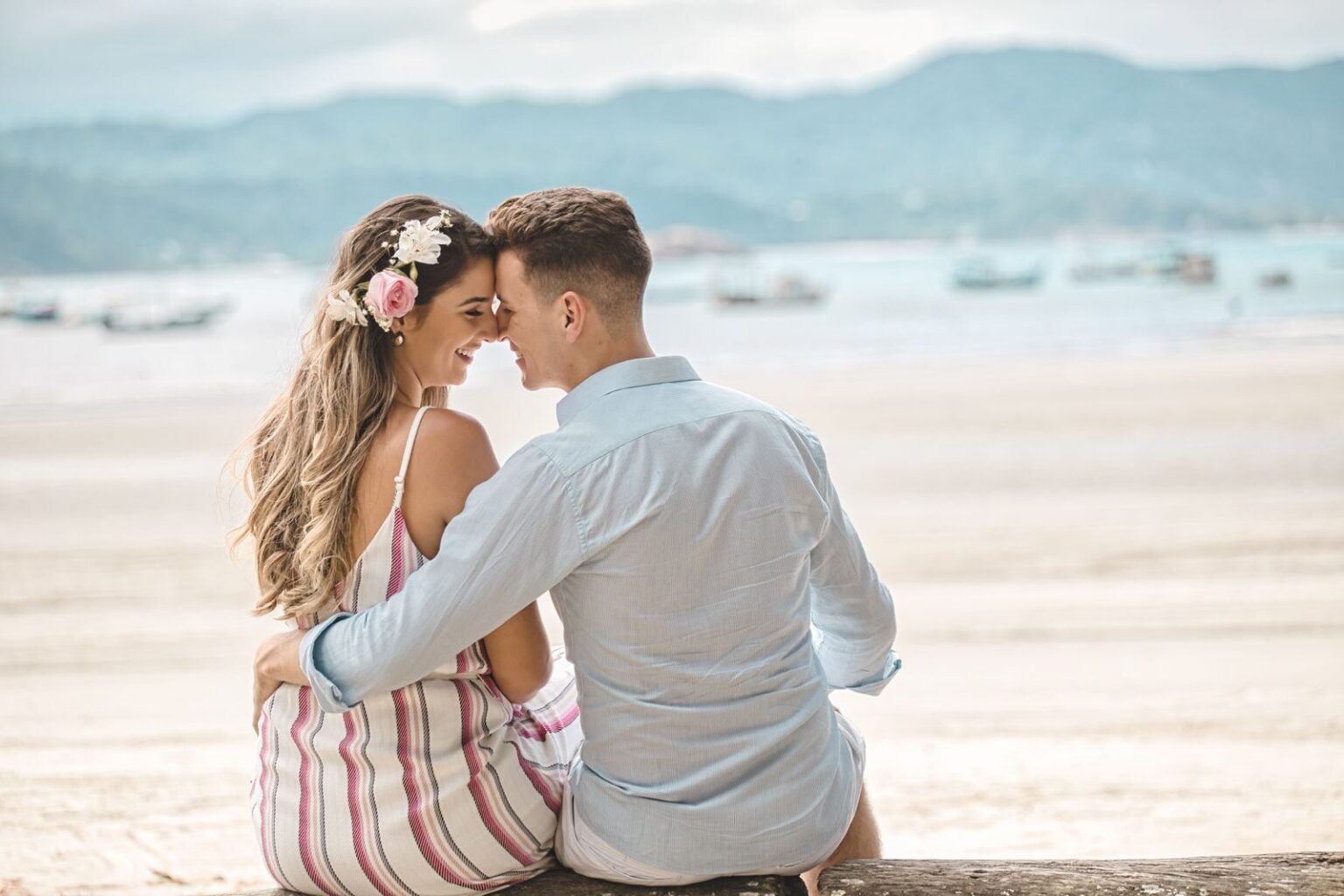 A romantic couple embraces on a scenic beach at sunset, highlighting affection and love.