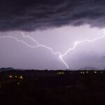 Dramatic nighttime capture of lightning striking over a rural landscape.