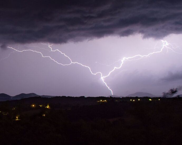 Dramatic nighttime capture of lightning striking over a rural landscape.