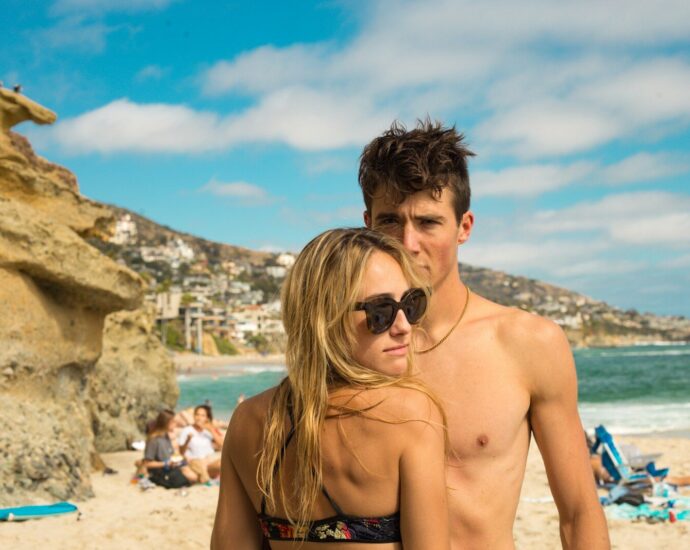 woman wearing sunglasses and bikini front of man standing near seashore
