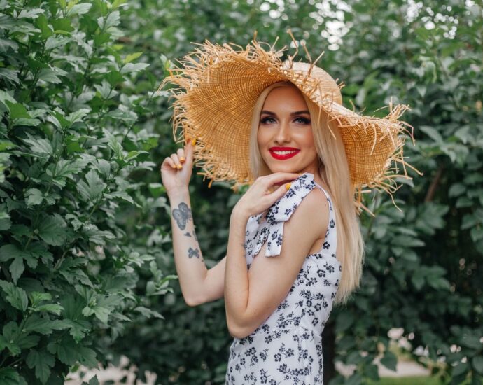 Charming blonde woman in a straw hat smiling outdoors in a floral sundress.
