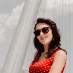 A woman in a red polka dot dress wearing sunglasses against a white bridge