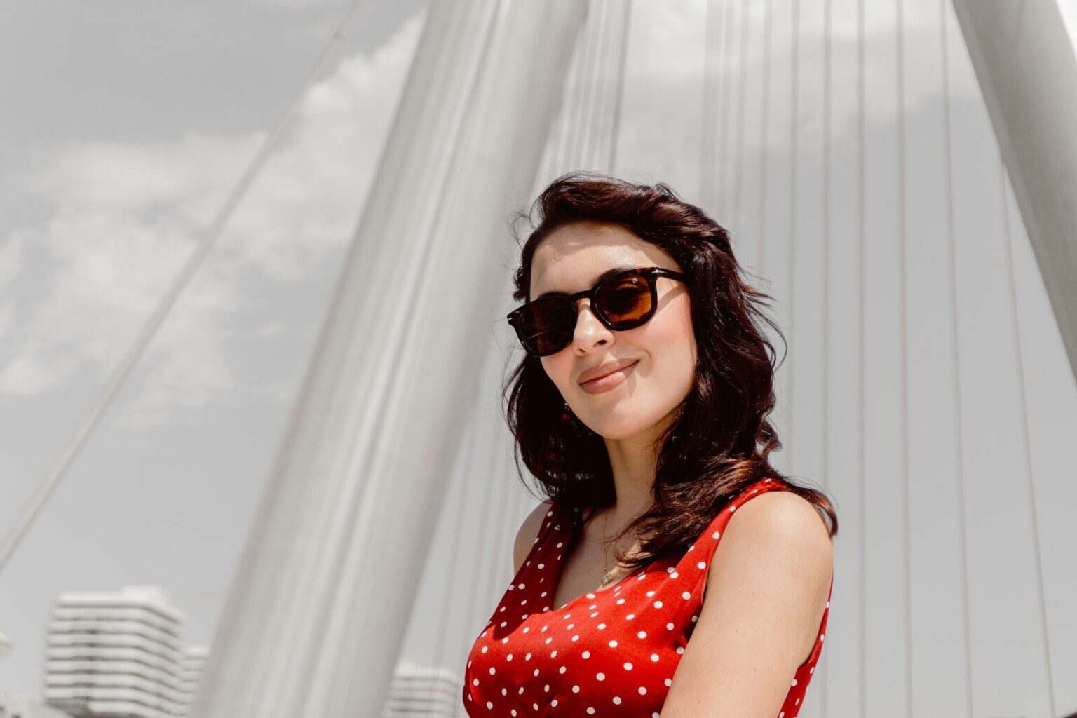 A woman in a red polka dot dress wearing sunglasses against a white bridge