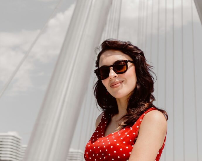 A woman in a red polka dot dress wearing sunglasses against a white bridge