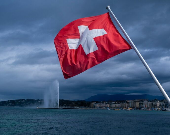 a swiss flag blowing in the wind near a body of water