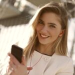 A smiling woman with headphones and smartphone enjoying music outdoors on a sunny day.