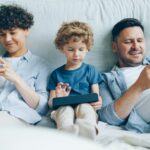 a man, woman and child sitting on a couch looking at their cell phones