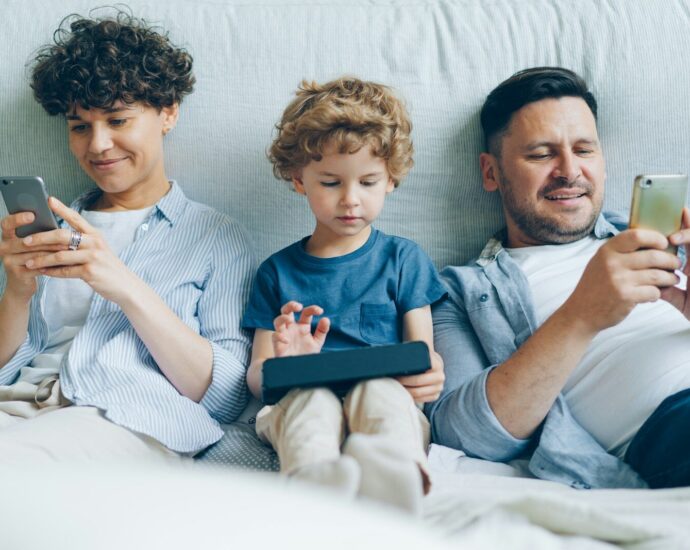 a man, woman and child sitting on a couch looking at their cell phones