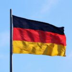 The flag of Germany waving on a metal pole against a blue sky