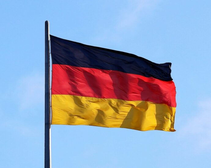The flag of Germany waving on a metal pole against a blue sky